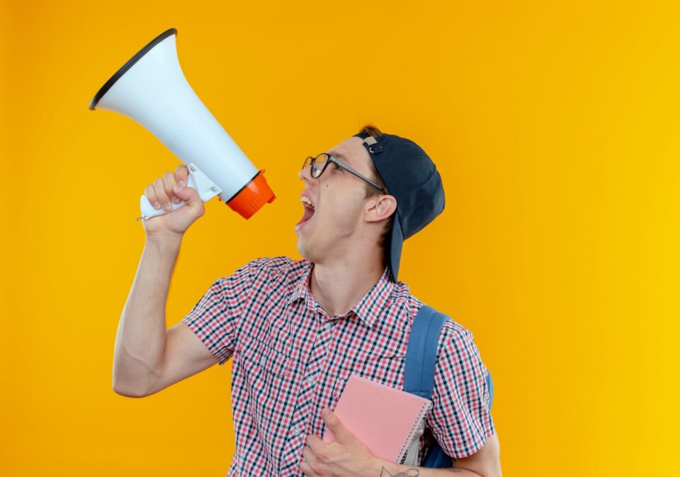 looking-side-young-student-boy-wearing-back-bag-glasses-cap-speaks-loudspeaker-holding-notebook (1)